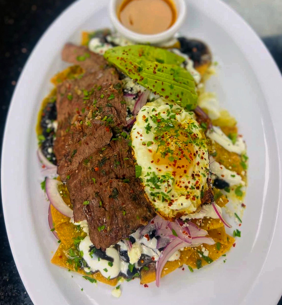 Green chilaquiles topped with steak, sunny-side-up eggs, and avocado at Leña Ardiendo Pizza in Cudahy.