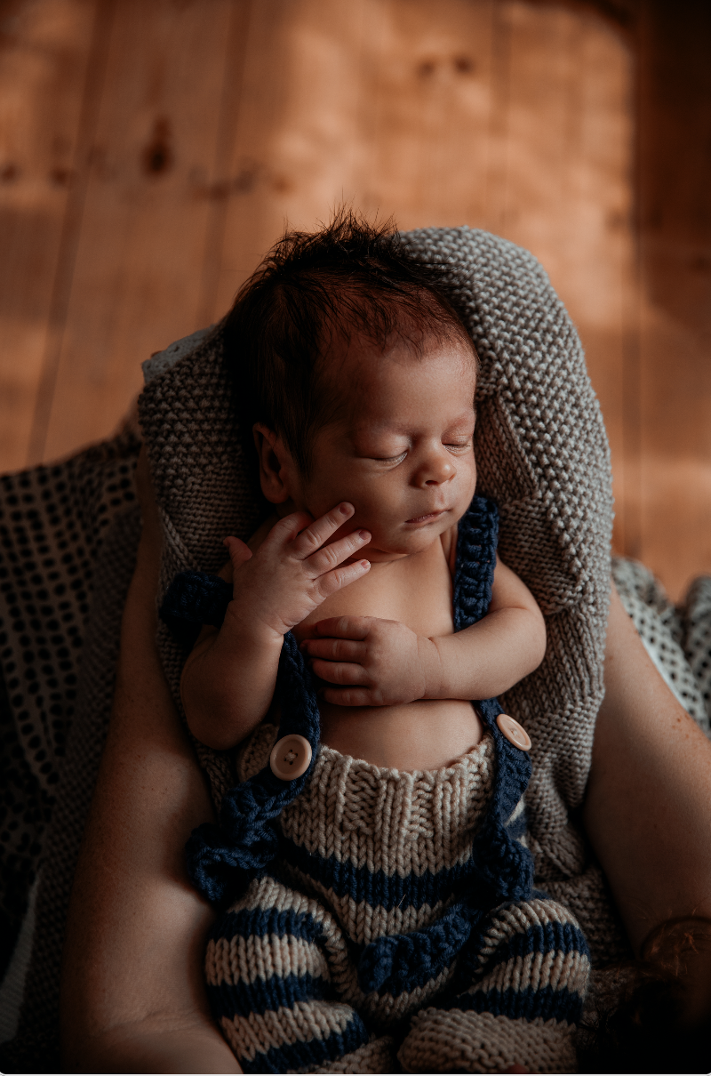 Newborn baby in hand knitted dungarees is asleep