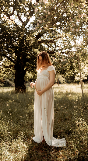 Pregnant mum in white dress stands in the meadow