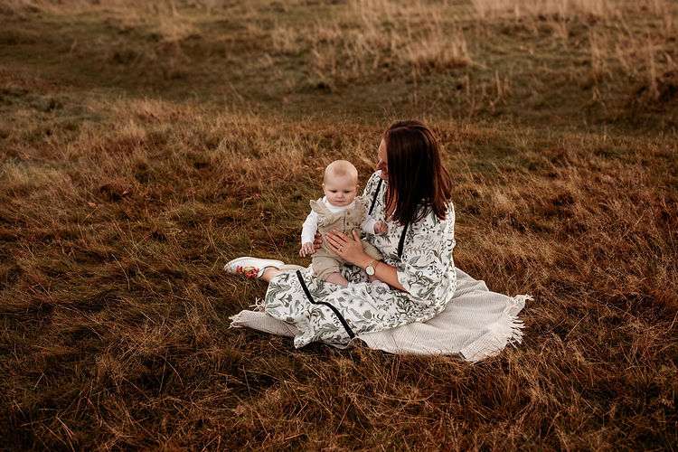 Mum and small daughter sit in the grass on blanket
