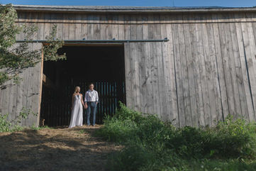 Bride and groom standing in the doorway of a rustic wooden barn, silhouetted against the light from inside.