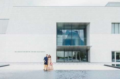Wide-angle wedding photography showing a couple standing by the reflecting pools with the "AGA KHAN MUSEUM" signage and white stone architecture in the background.