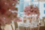 Elegant table setting with pink floral centerpiece, surrounded by chairs. Large windows and cityscape in the background. Table number 4 visible.