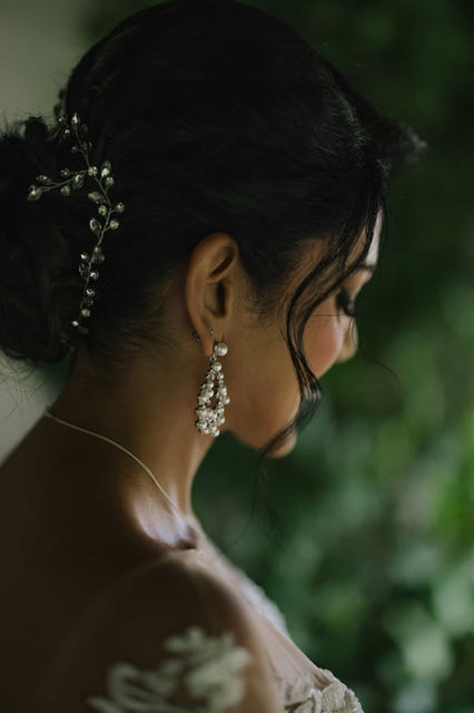 A soft, close-up profile portrait of a bride looking downward, highlighting her elegant drop earrings and intricate bridal hairstyle.