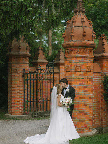 A romantic portrait of a bride and groom kissing in front of the iconic, ornate red brick columns and historic wrought-iron gate at Guild Park and Gardens.