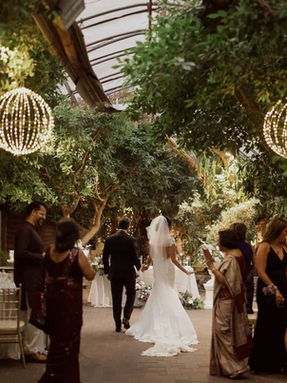A bride and groom make their grand entrance into a lush, greenery-filled conservatory wedding reception venue in Toronto.