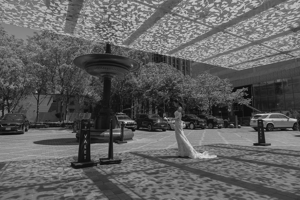 Black and white outdoor portrait of a bride walking through a sun-dappled Four Seasons Hotel in Yorkville courtyard with patterned shadows.