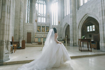 Fine art wedding photo of a bride with a flowing cathedral-length veil standing at the altar steps of Trinity College Chapel, looking toward the ornate altarpiece.