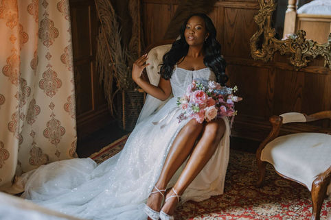 A bride posing elegantly in a wedding gown with a thigh-high slit, sitting in a historic dark wood room.