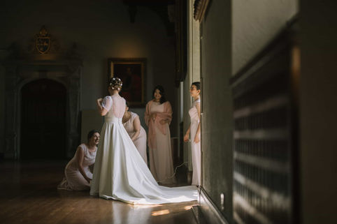 Moody candid wedding photograph of a bride and her wedding party in a historic Toronto library, softly lit by natural window light.