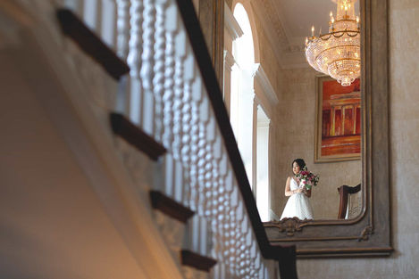 Creative editorial Toronto wedding photo using reflection to capture the bride near a grand staircase and chandelier.