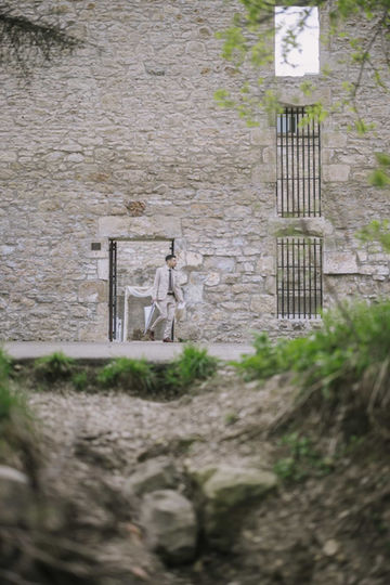 A creative architectural wedding shot showing a small bride and groom standing inside the doorway of an ancient, textured stone wall and ruins.