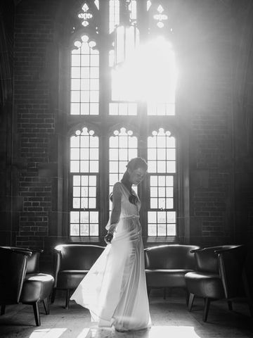High contrast black and white bridal portrait of a bride standing gracefully in front of grand architectural Gothic windows.
