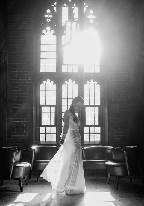 High contrast black and white bridal portrait of a bride standing gracefully in front of grand architectural Gothic windows.