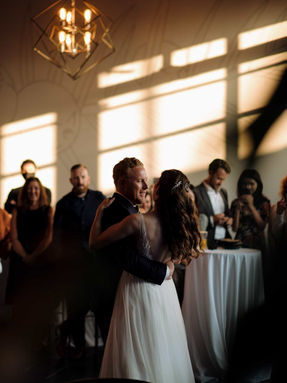 A moody, artistic shot of a couple sharing a romantic dance as warm sunlight casts long shadows across the reception floor.