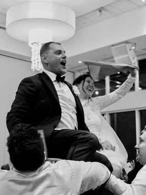 High-energy black and white photo of a groom being lifted on a chair and cheering during the traditional Jewish Hora dance.
