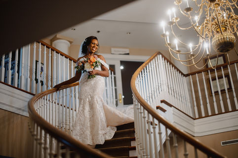 A beautiful portrait of the bride smiling and looking down, holding her bouquet on a grand staircase, a timeless shot often seen in classic Niagara wedding photos.