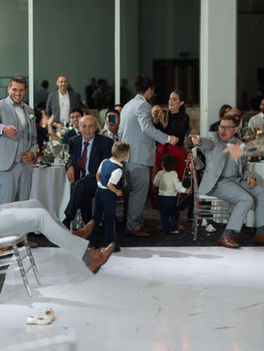 A fun, candid reception photograph of wedding guests dropping low to the white dance floor during a high-energy party.