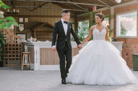 A happy bride in a full ballgown and her groom holding hands while walking past a rustic white wooden indoor bar setup.
