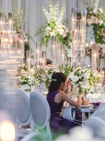 An elegant and luxurious wedding reception layout inside the grand ballroom at The Arlington Estate, featuring towering glass cylinder candles and opulent white floral installations.