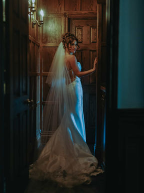 Moody interior bridal portrait of a bride looking over her shoulder through an elegant, dark wood-paneled doorway inside the historic manor house at Erin Estate.