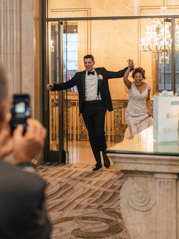 A joyous bride and groom holding hands and cheering as they make their grand entrance into their wedding reception.