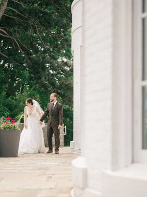 Candid shot of a bride and groom holding hands while walking past large planters on a stone terrace at a classic Toronto estate.