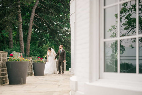 Candid shot of a bride and groom holding hands while walking past large planters on a stone terrace at a classic Toronto estate.