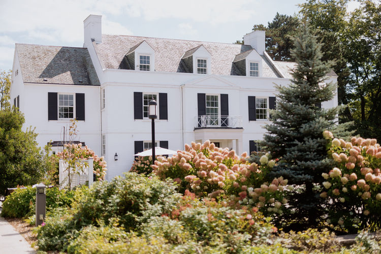 The grand exterior of a white historic mansion surrounded by lush green gardens, a perfect setting for a Mississauga wedding photographer