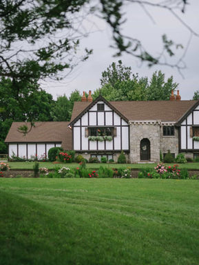 Wide-angle landscape photograph showcasing the iconic white and black half-timbered English Tudor mansion and vast manicured green lawns at Erin Estate.
