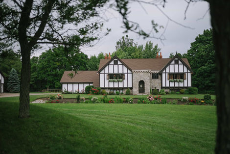 Wide outdoor view of the historic Tudor-style manor at Erin Estate with manicured green lawns and surrounding forest.