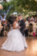 A couple is joyfully lifted in chairs during a celebration. They smile broadly under a bright chandelier in a festive indoor setting.