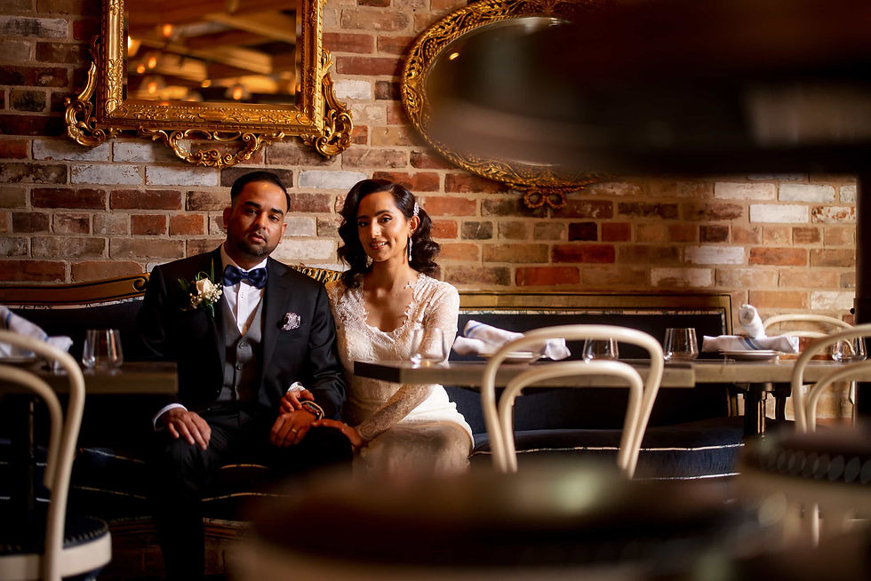 Man and woman holding hands, smiling at each other in a cozy cafe. Brick wall and warm lighting create an intimate setting.