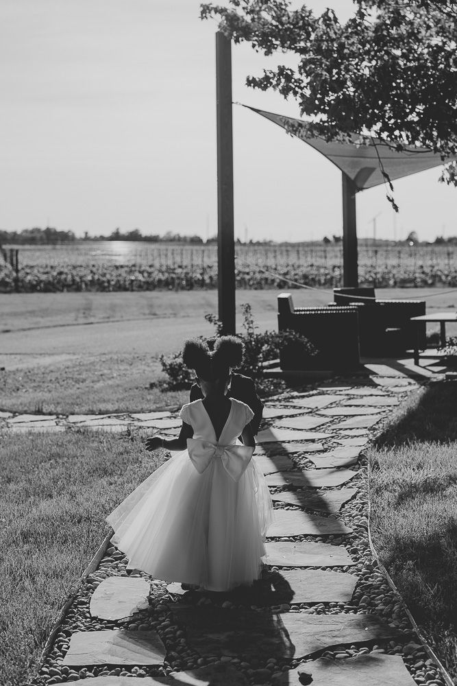 Candid black and white photo of a young flower girl in a tulle gown walking down a stone path at Château des Charmes in Niagara-on-the-Lake