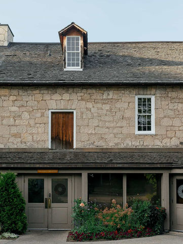 Exterior architectural photograph of the historic multi-story 19th-century limestone mill building and manicured entrance gardens at Ancaster Mill.