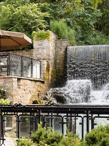 A spectacular wide-angle view of the venue's iconic natural rushing waterfall flowing beneath stone terrace walls and an outdoor patio balcony.