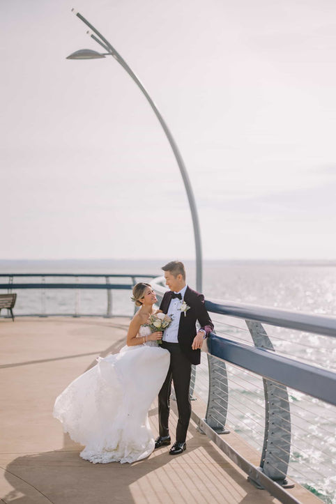 Bride and groom leaning against the railing on Brant Street Pier beneath a modern curved streetlamp in Burlington.