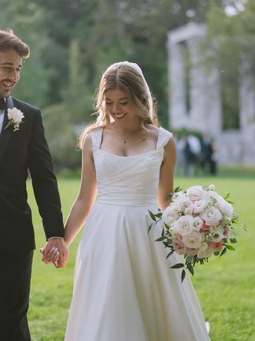 Joyful candid shot of a bride and groom holding hands and smiling while walking across the open green lawns, with the historic white Grecian columns softly blurred in the background.