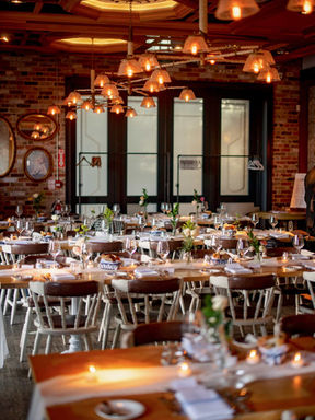 A vertical interior shot highlighting rows of decorated guest tables beneath a striking ceiling arrangement of glowing copper pendant lamps.