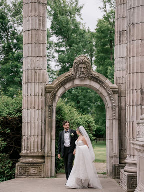 A bride and groom posing elegantly together beneath a massive carved stone monument arch at Guild Park in Toronto.