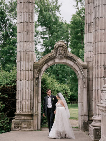 A bride and groom posing elegantly together beneath a massive carved stone monument arch at Guild Park in Toronto.