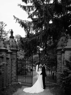 A timeless black and white fine-art photograph of a bride and groom embracing next to classic wrought iron gates at Guild Park.