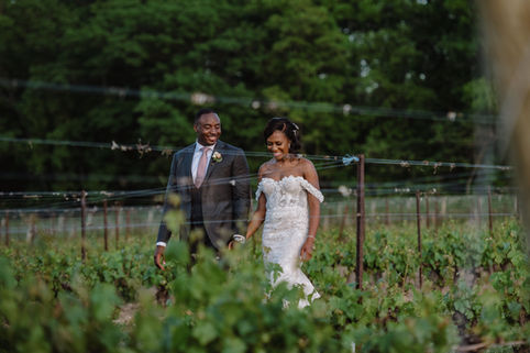 A candid and happy photo of the bride and groom walking hand-in-hand through rows of grapevines, highlighting the beauty and romance of a Niagara winery wedding.