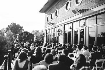 A timeless black and white documentary photograph capturing a massive guest crowd watching a wedding ceremony outside the modern estate pavilion.