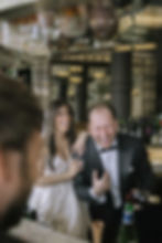 A bride and groom share an emotional moment in a church, with colorful stained glass in the background. Bride is holding the groom's face.