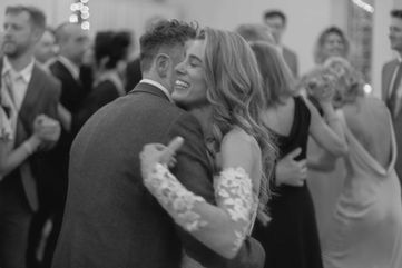 Black and white candid photo of a bride and groom dancing joyfully in a crowd of guests at a Toronto wedding reception.