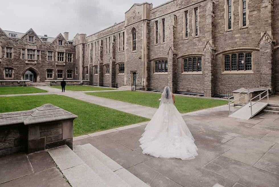 A Toronto wedding photographer captures a bride in a grand ballgown with a long lace train standing against the historic stone architecture of a Gothic-style manor.