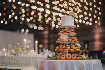 Close-up shallow depth of field photograph of a modern multi-tiered donut tower wedding cake display with a background of glowing golden fairy light bokeh at York Mills Gallery.