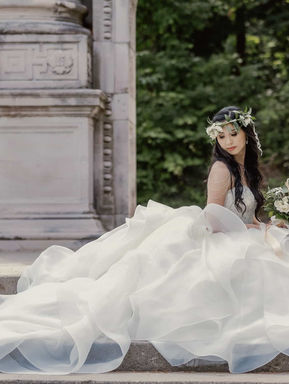 A bride in a grand wedding gown sitting gracefully on the base of a massive, historic carved stone monument at Guild Park.