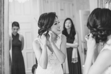Candid black and white wedding photography of a bride putting on her earrings while getting ready inside the elegant dressing room at Graydon Hall Manor.